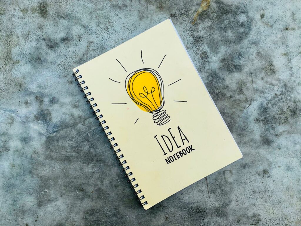 Top view of creative spiral notebook with yellow light bulb illustration on cover placed on gray table